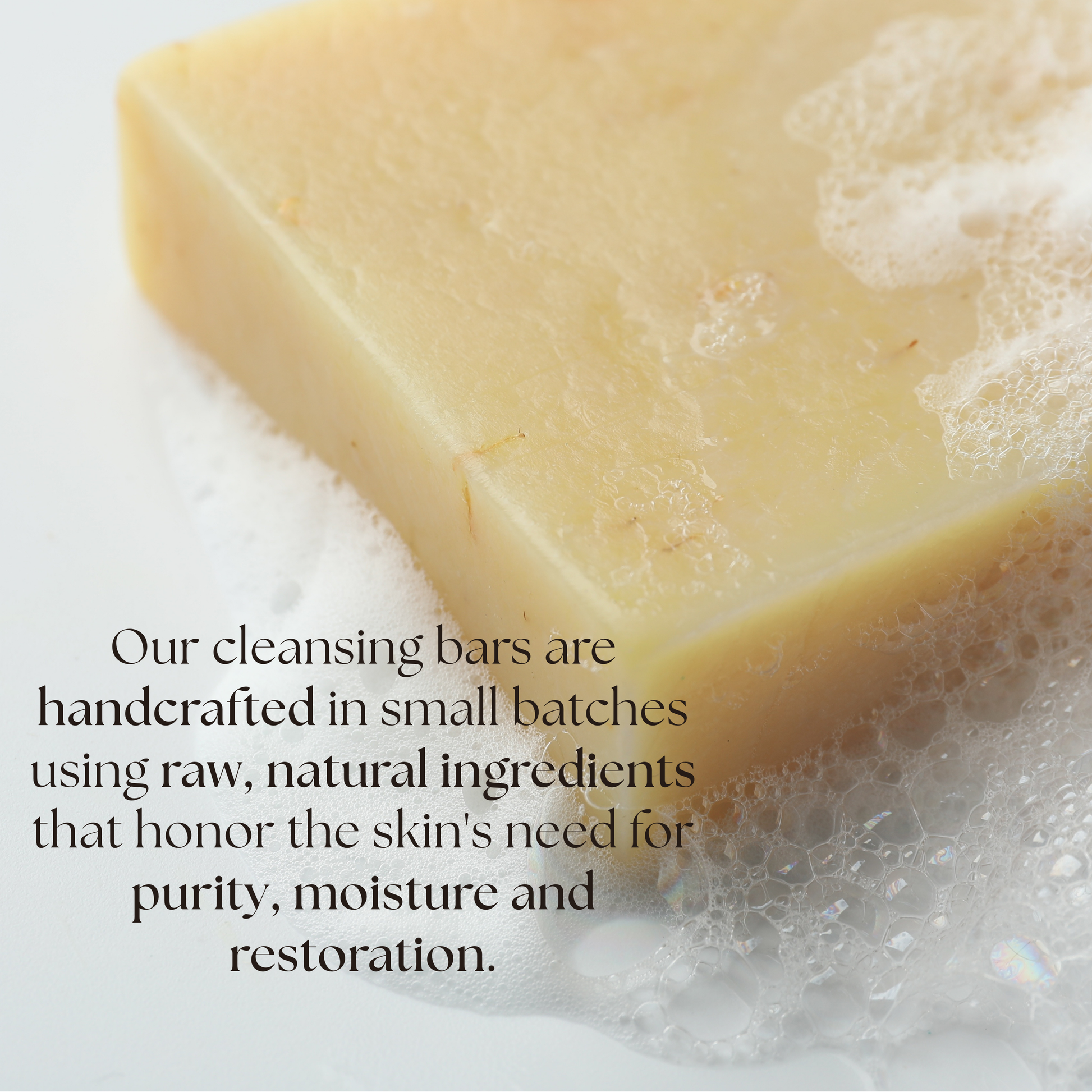Bar of soap with bubble lather featuring text about handcrafted cleansing bars made with raw ingredients to honor skin's need for purity, moisture and restoration.
