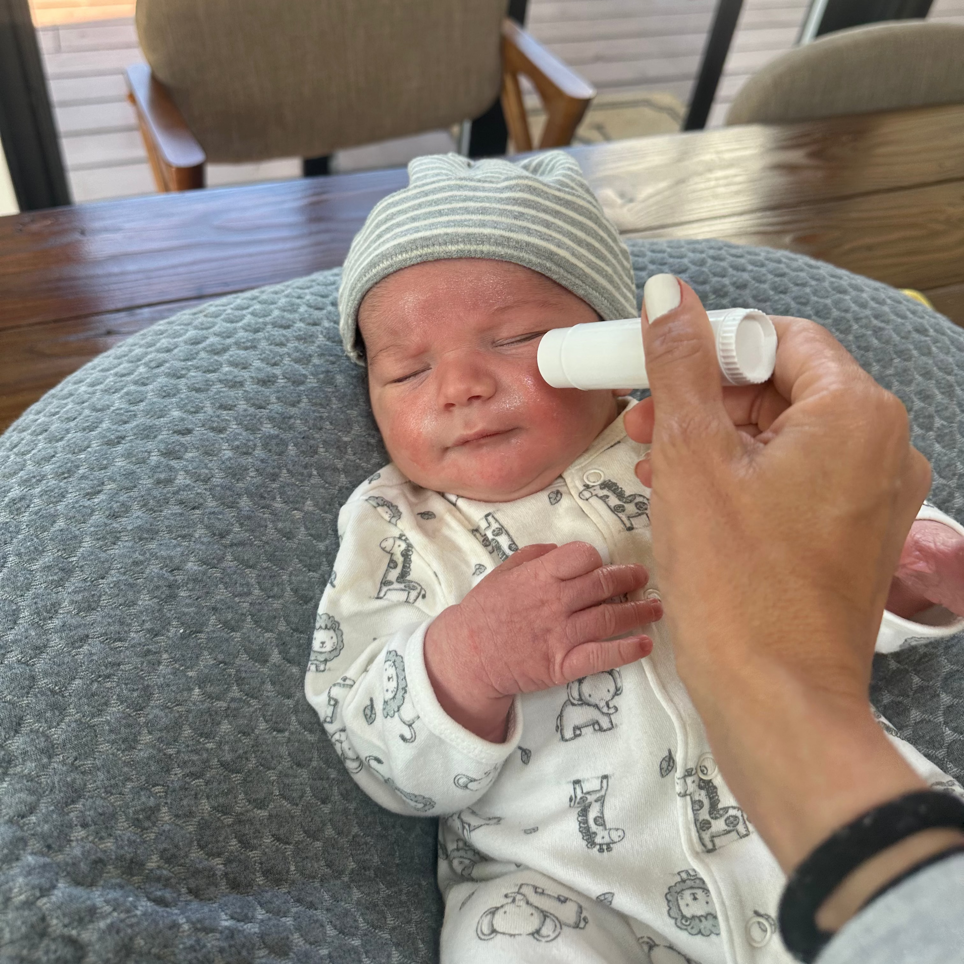 Newborn baby being held on a cushioned chair with a person using a moisture stick on the baby's face.